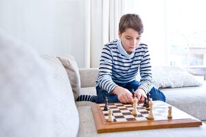 Serious looking boy wearing striped t-shirt sitting on sofa looking at chess board