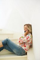 Pretty blonde woman wearing floral pattern top sitting on staircase talking on phone