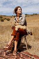 Pretty woman sitting on stool in steppe with a lion cub on her lap, Africa