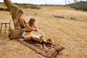 Happy woman sitting on steppe and playing with lion cub, laughing