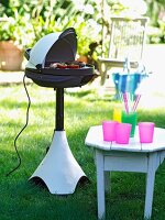Electric grill and stool with plastic cups in garden