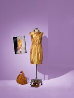 Gold silk taffeta dress on mannequin with bag and shoes on side