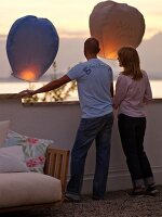 Couple standing on balcony and watching sky lanterns at dusk