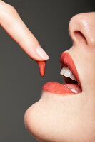 Drop of lipstick dripping from woman's finger to her lips, close-up