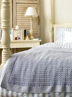 Close-up of bed with blue and white striped linen bed sheet and crochet blanket