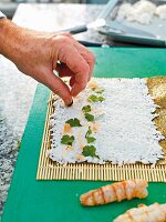 Sushi being prepared: sushi rice being spread on a bamboo mat and topped