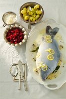 Blue carp with lemon slices and horseradish sauce on plate, bowls of beetroot and potatoes