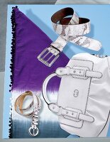 White ivory bag, purple batik cloth and leather belt on blue background