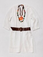 Close-up of white tunic, leather belt, necklaces with gemstone and shell