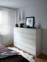 White drawer chest with photo frames, table lamp and decorations in bedroom