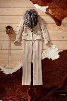 Beige trouser suit with fur collar and small wall clock on wooden floor