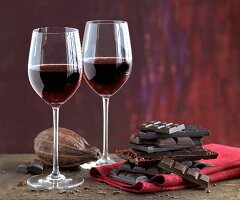 An arrangement of red wine glasses, cocoa beans and a stack of chocolate