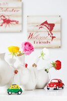 Roses in white vases with small pendants behind toy cars