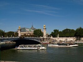 Ferry passing below of Pont Alexandre III over Seine river in Paris, France