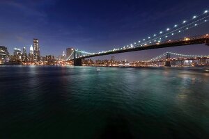 View of Brooklyn Bridge on East River at night in Manhattan, New York, USA