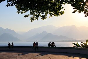 People sitting at promenade near sea and mountain range in Antalya, Turkey