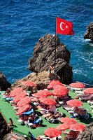 Turkish flag and people relaxing on sun loungers near sea in Antalya, Turkey