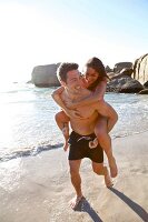 Man carrying woman on piggyback and running on the beach along the sea shore