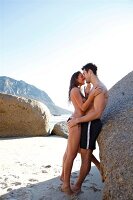 Seductive couple embracing each other and leaning against rock on beach