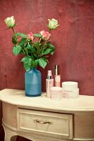 Cosmetics on dresser next to roses in vase