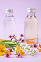 Aromatherapy glass bottles with essential oils and flowers scattered on purple background