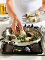 Close-up of hand roasting cod fish with vegetables in wok