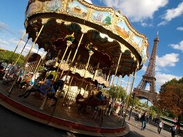 People in flying horse carousel across Eiffel Tower in Paris, France