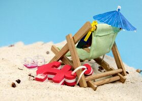 Liegestuhl, Anker, Sonnenschirm und Flip Flops im Sand