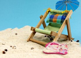 Liegestuhl mit Flip Flops und Sonnenschirm im Sand