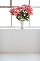 Vase with pink peonies on window sill