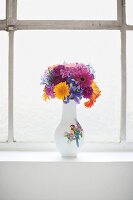 Vase with different types of flowers on window sill