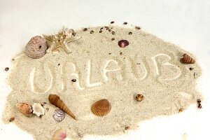 "Urlaub" im Sand geschrieben mit Muscheln drum herum