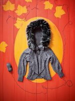 Crochet sweater with faux fur hood on wooden surface