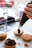 Half macron being filled with chocolate cream using icing bag