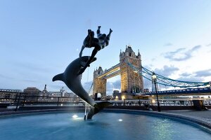 Sculpture of dolphin with girl and Tower Bridge in background at Southwark, London, UK