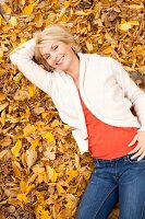 Blonde Frau in heller Jacke liegt auf Herbstlaub