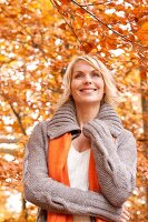 Contemplative blonde woman wearing gray cardigan smiling in autumn forest