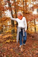 Blonde woman wearing orange scarf and bright sweater walking in autumn forest, smiling