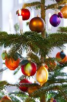 Close-up of Christmas tree decorated with baubles, lit candles and fruits