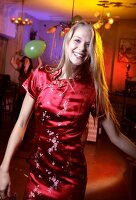 Happy woman wearing red satin dress celebrating while dancing at New Year's Eve party