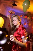 Happy woman wearing red satin dress celebrating while dancing at New Year's Eve party