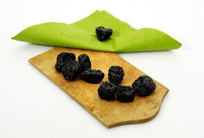 Dry plums on wooden platter with green cloth on white background