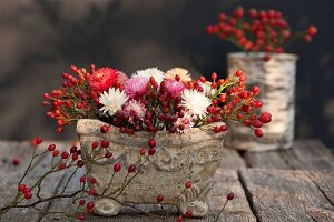 Hagebutten und bunte Strohblumen in einer Vase aus Stein