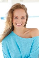 Portrait of beautiful blonde woman wearing turquoise top, smiling