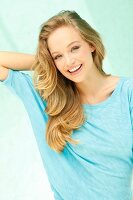 Portrait of beautiful blonde woman wearing turquoise top with hand behind head, smiling