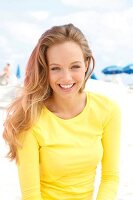 Portrait of happy blonde woman with long hair wearing yellow t-shirt, laughing 