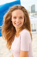 blonde Frau lacht in die Kamera im rosa T-Shirt am Strand