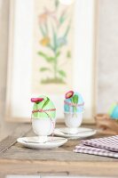Colourful Easter eggs in egg cups decorated with daisies and ribbons
