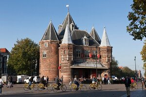 Tourists standing and cycling outside Waag monument in Nieuwmarkt, Amsterdam, Netherlands