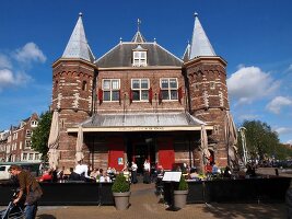 Tourists standing and cycling outside Waag monument in Nieuwmarkt, Amsterdam, Netherlands